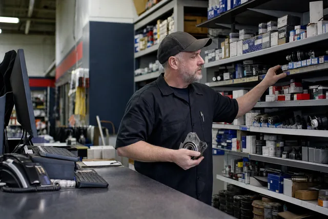 A parts man pulling a box off the shelf behind a parts counter