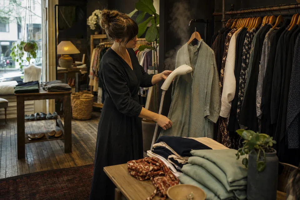 A shop owner steaming a jacket beside the racks in a clothing boutique
