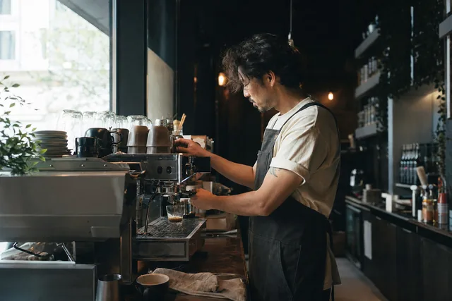 A barista pulling a shot on the espresso machine behind a cafe counter