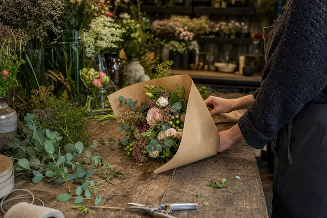 A florist wrapping a finished bouquet in paper on a workbench