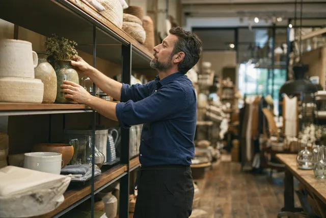 A shopkeeper straightening pottery on the shelves of a home goods store
